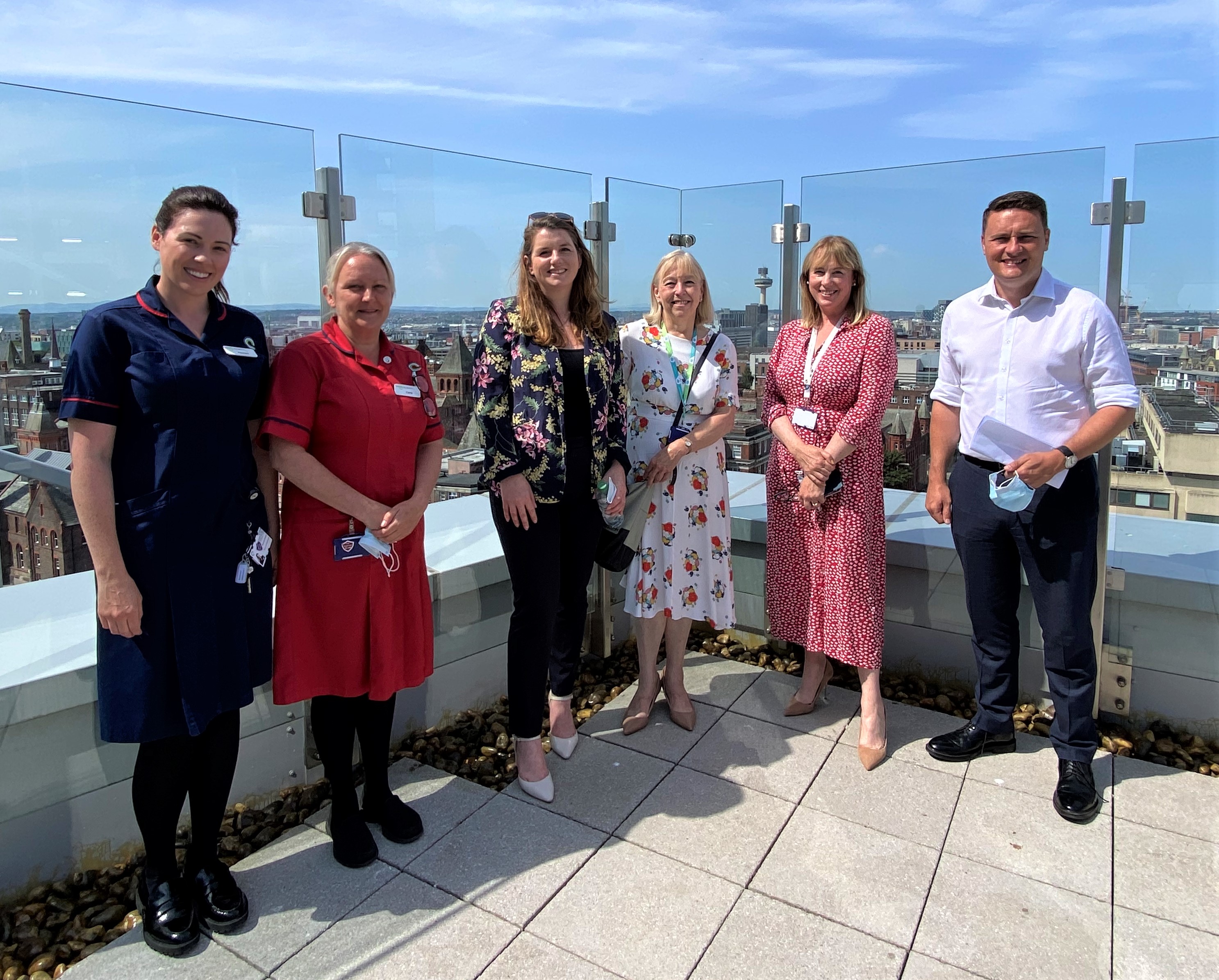 A picture of people smiling on the rooftop terrace outside Chemotherapy at Clatterbridge Cancer Centre - Liverpool. The picture shows Chemotherapy ward manager  Rachael Gregory, Matron Carla Taylor, Alison McGovern MP, Trust Chair Kathy Doran, Chief Executive Liz Bishop and Shadow Health Secretary Wes Streeting