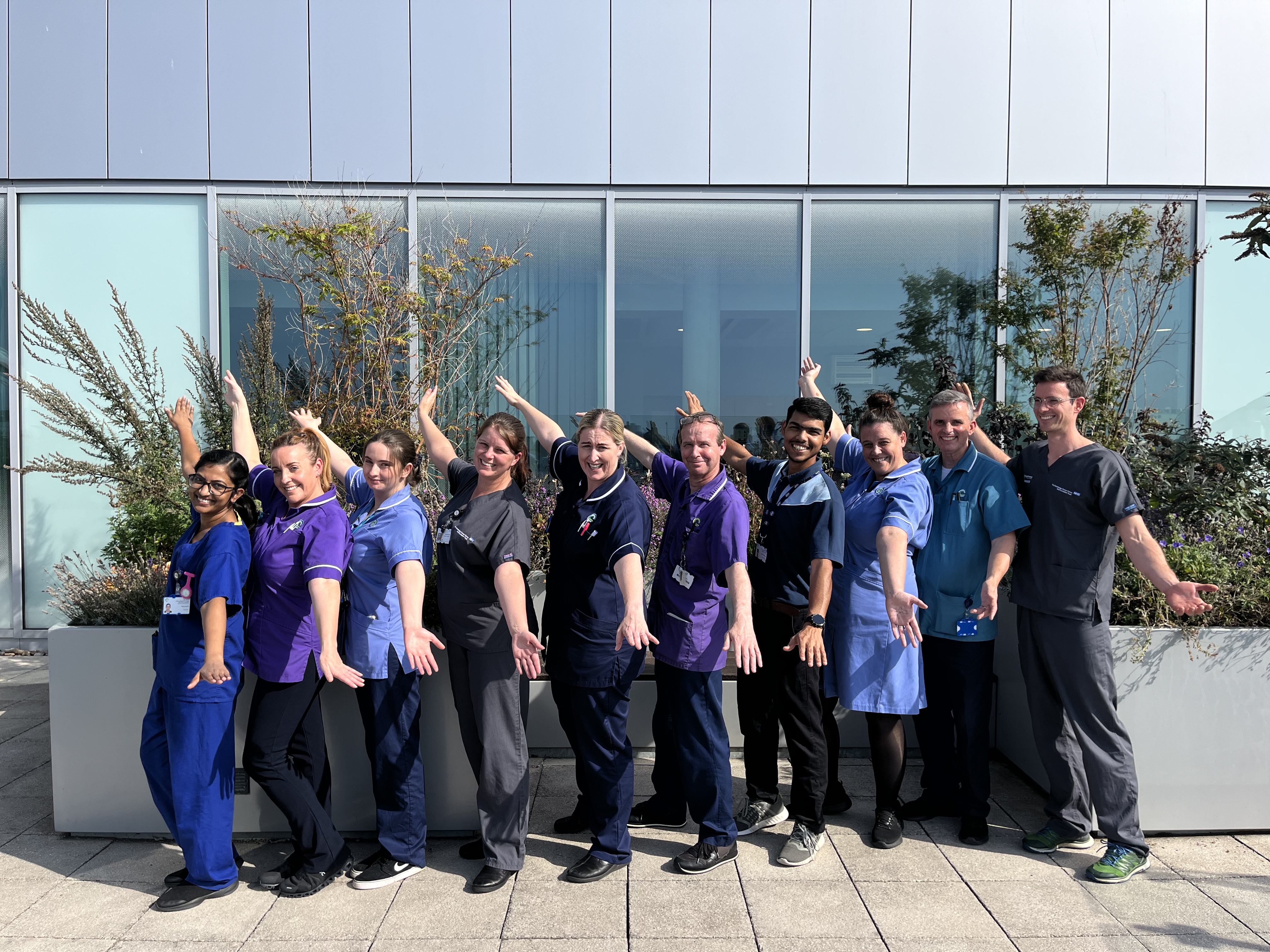 Picture of a variety of ward staff. They are in a line on the hospuital roof terrace and are waving their arms in celebration