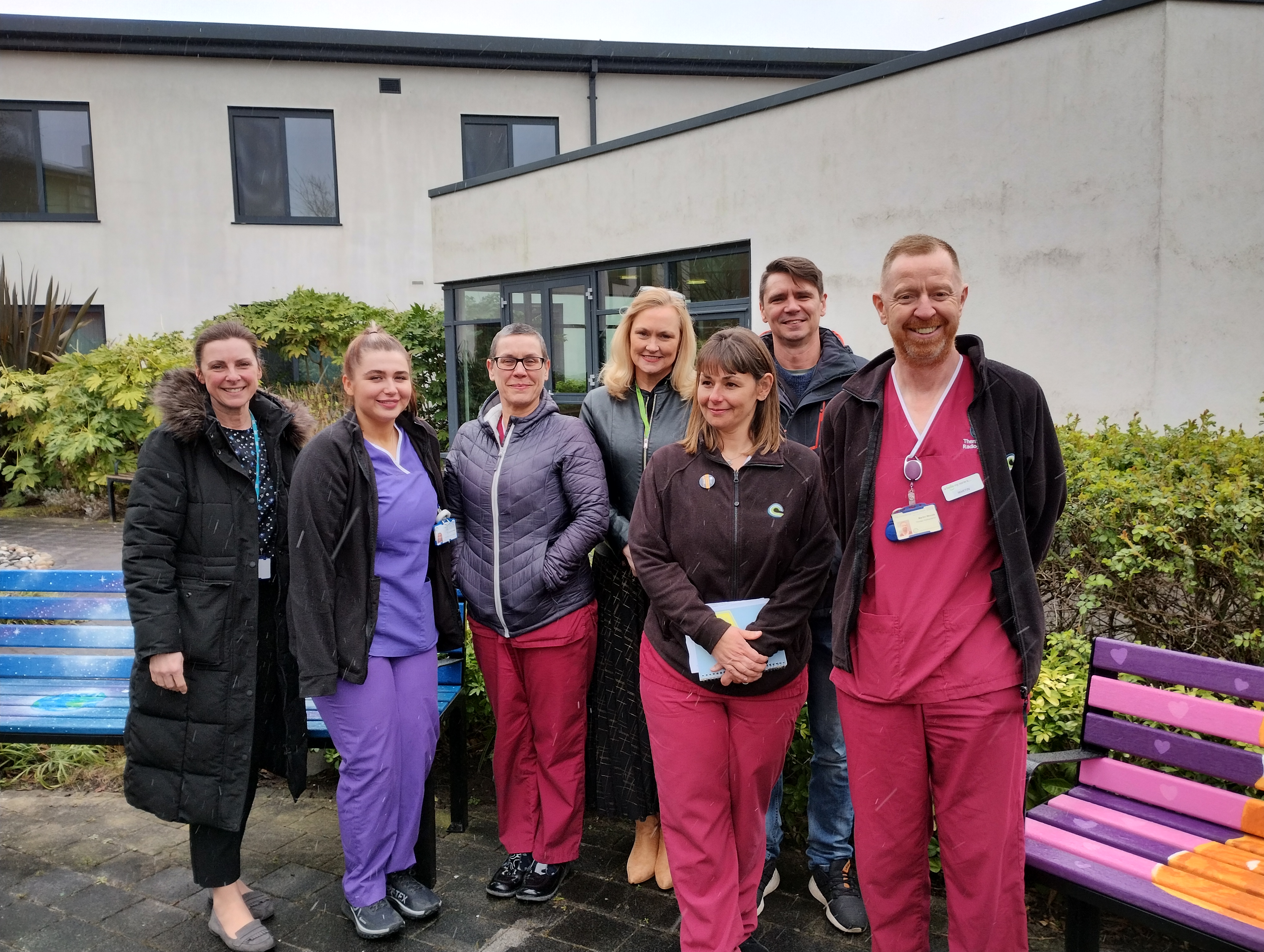 Picture of Radiotherapy staff and artist Ian Ryall in the courtyard garden at CCC-Aintree with the colourful memorial benches