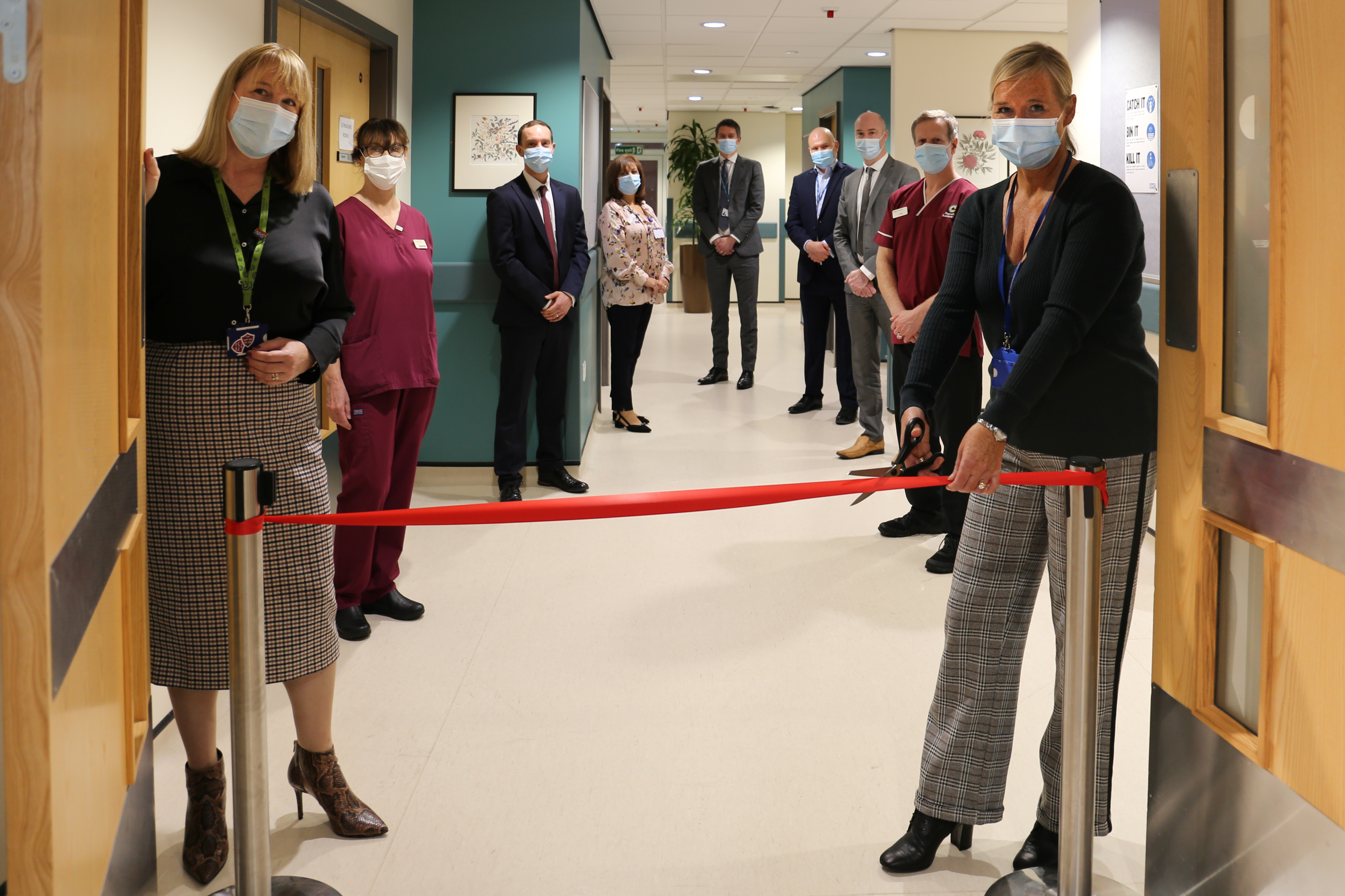 Liz Bishop (Chief Executive of The Clatterbridge Cancer Centre) and Janelle Holmes (Chief Executive of Wirral University Teaching Hospital) are pictured opening the new Clatterbridge Diagnostics centre. Janelle is cutting a ribbon. They are surrounded by other staff.