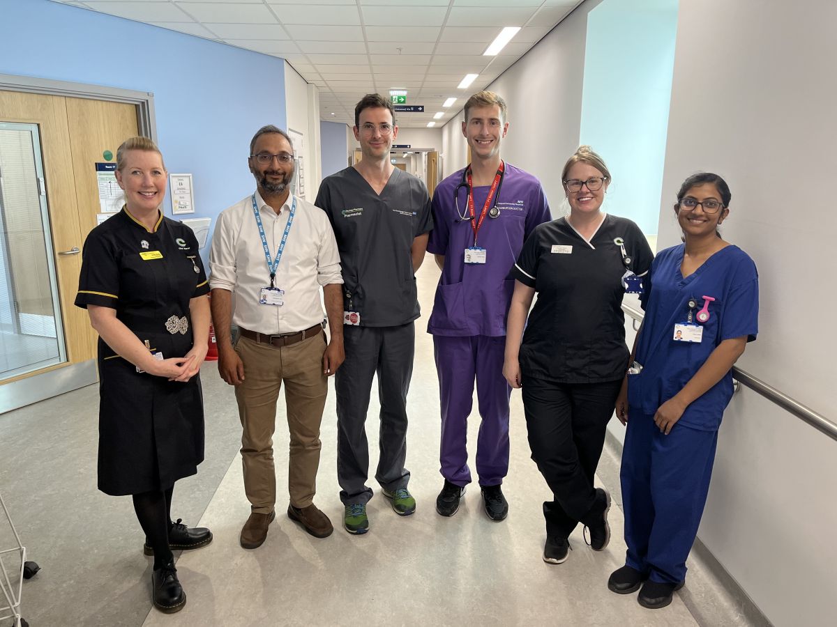 Picture of Chief Nurse Julie Gray (on left) with a mix of ward staff in different uniforms. They are in a hospital corridor and are all smiling